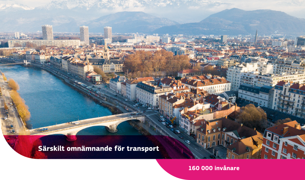 Flygfoto över Grenoble med byggnader, en flod med en anslutande bro och vita berg i bakgrunden